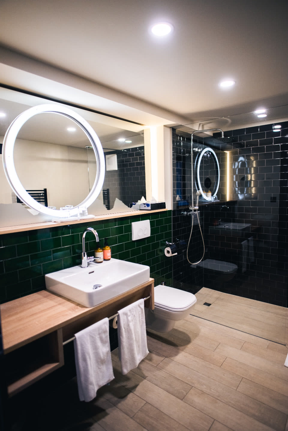 Bagno con piastrelle verde scuro e specchio rotondo illuminato